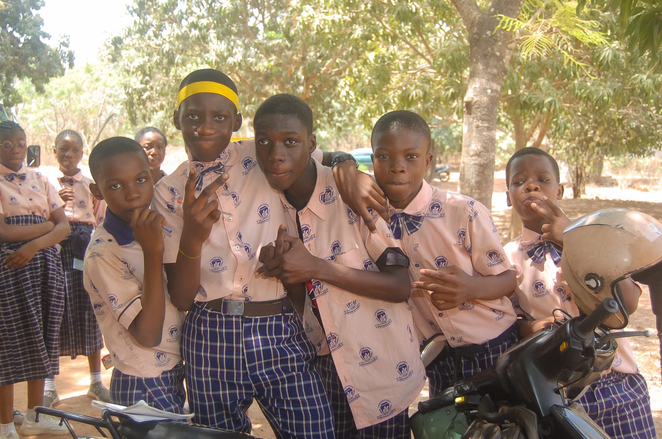 Cinq garçons en uniforme scolaire, bras dessus bras dessous, prennent la pose sous une lumière tachetée lors d’une sortie éducative.