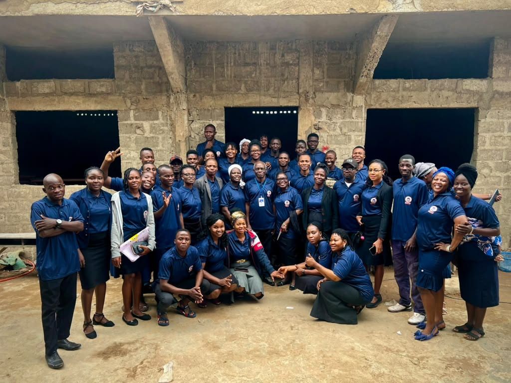 L’équipe de Champions Schools Parakou, un groupe nombreux en polo bleu marine floqué, réuni sous une travée ouverte d’un bâtiment en blocs inachevé.